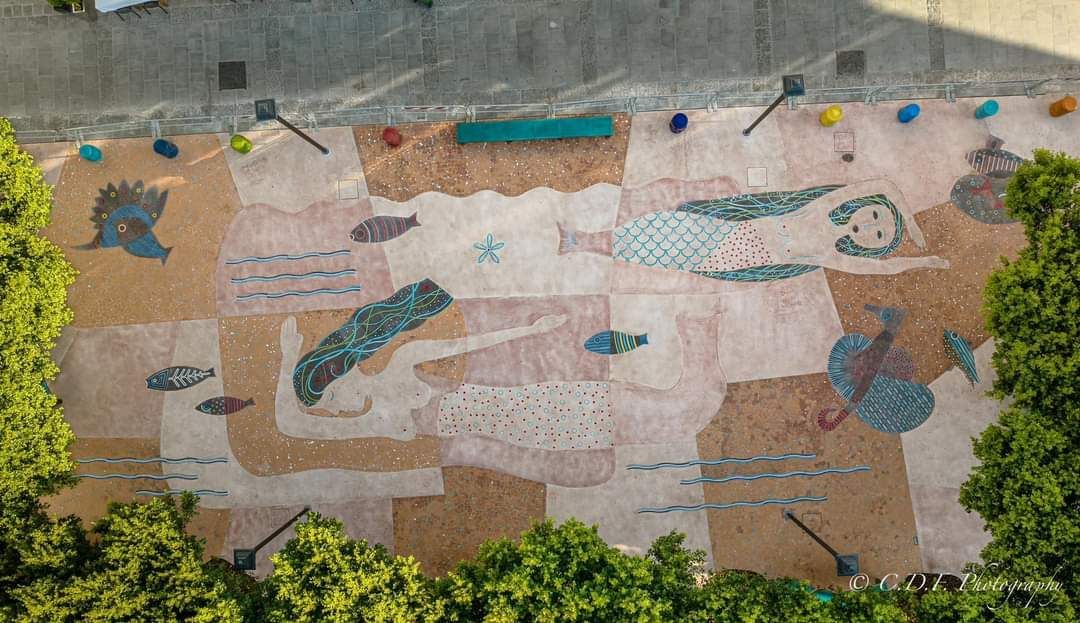 Una veduta aerea di un dipinto di una sirena a terra in un parco circondato da alberi.