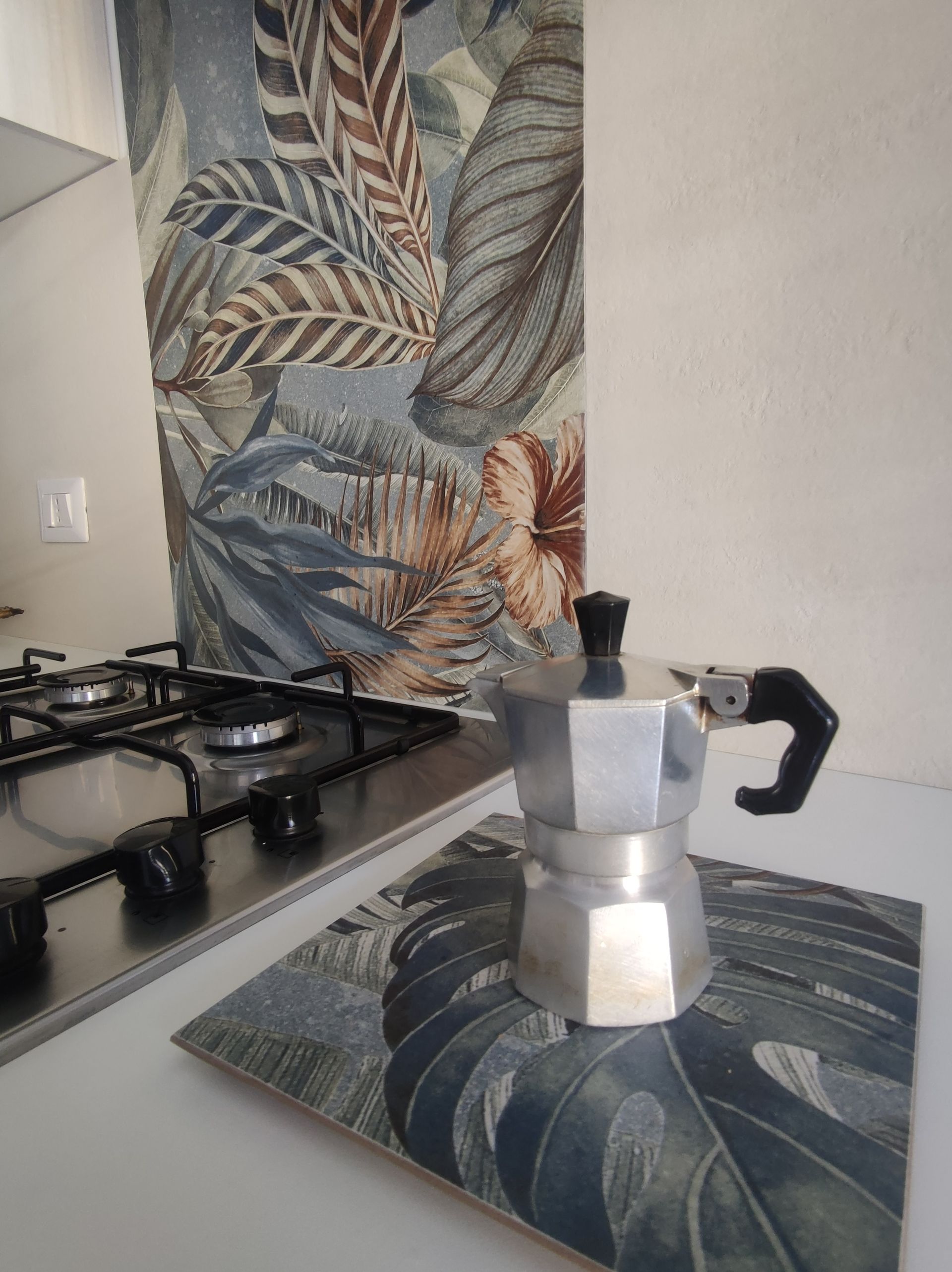 Una caffettiera è appoggiata su un fornello, accanto a un muro ricoperto di foglie.