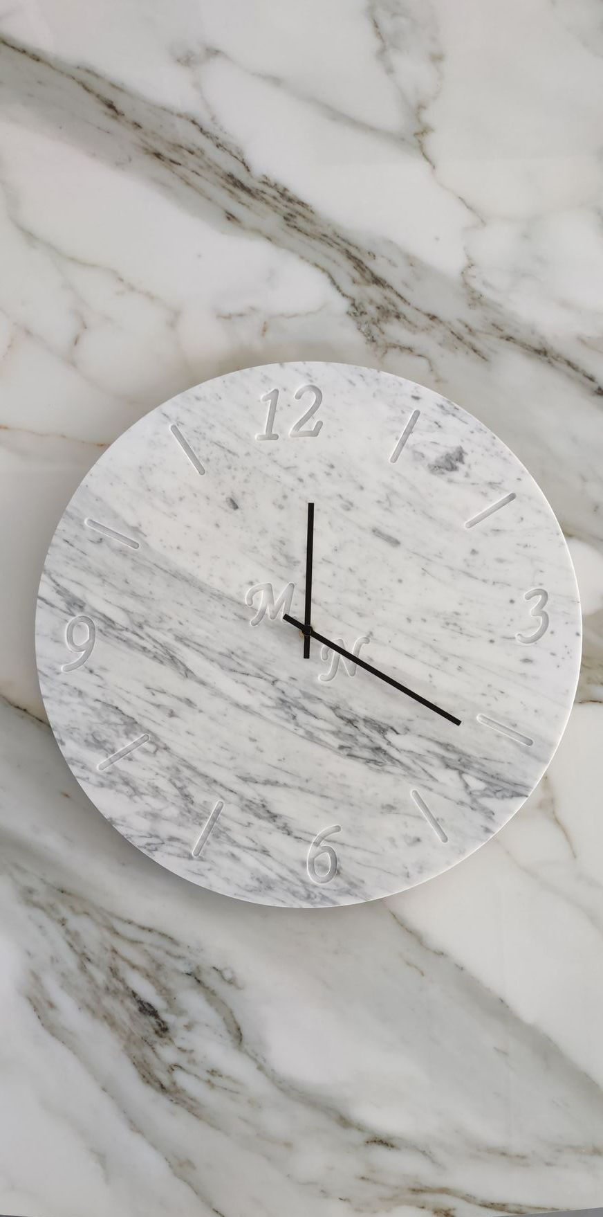 Un orologio di marmo bianco è appeso a una parete di marmo.