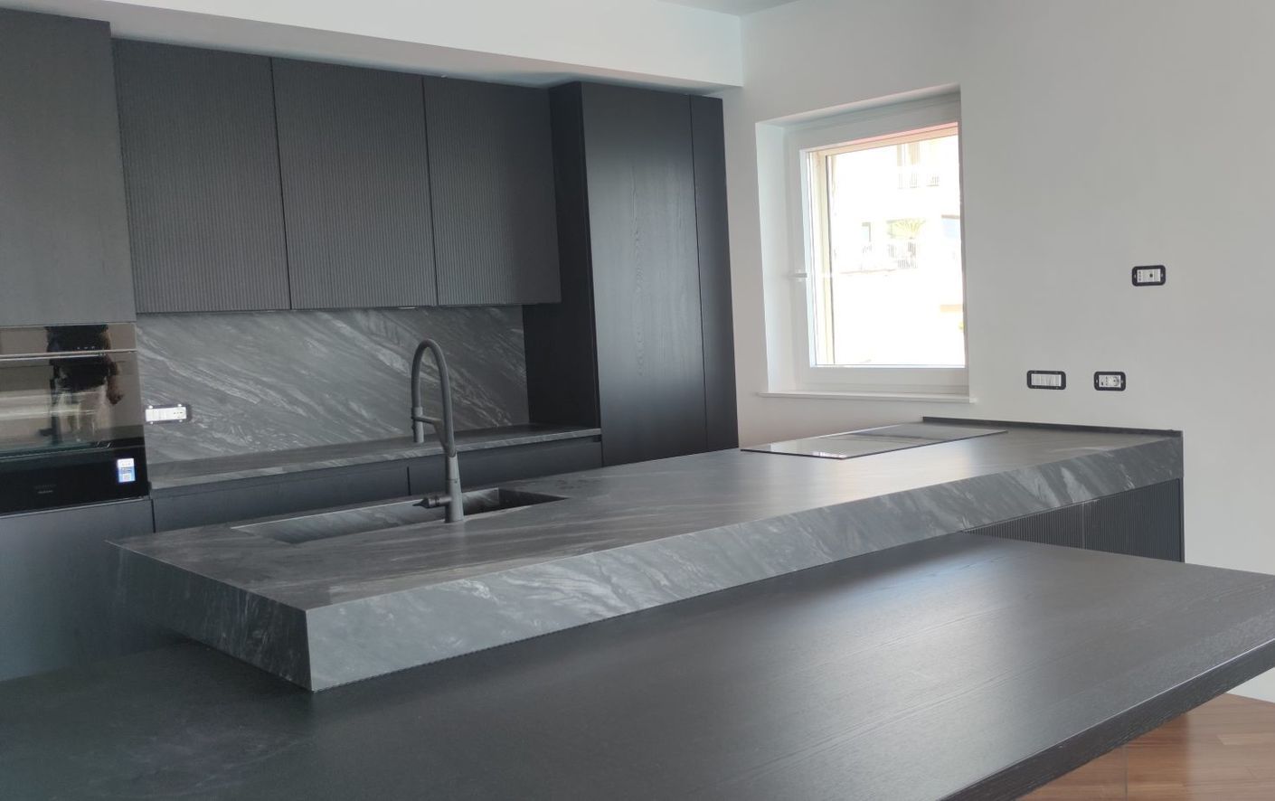 Una cucina con mobili neri, un piano di lavoro nero, un lavandino e una finestra.