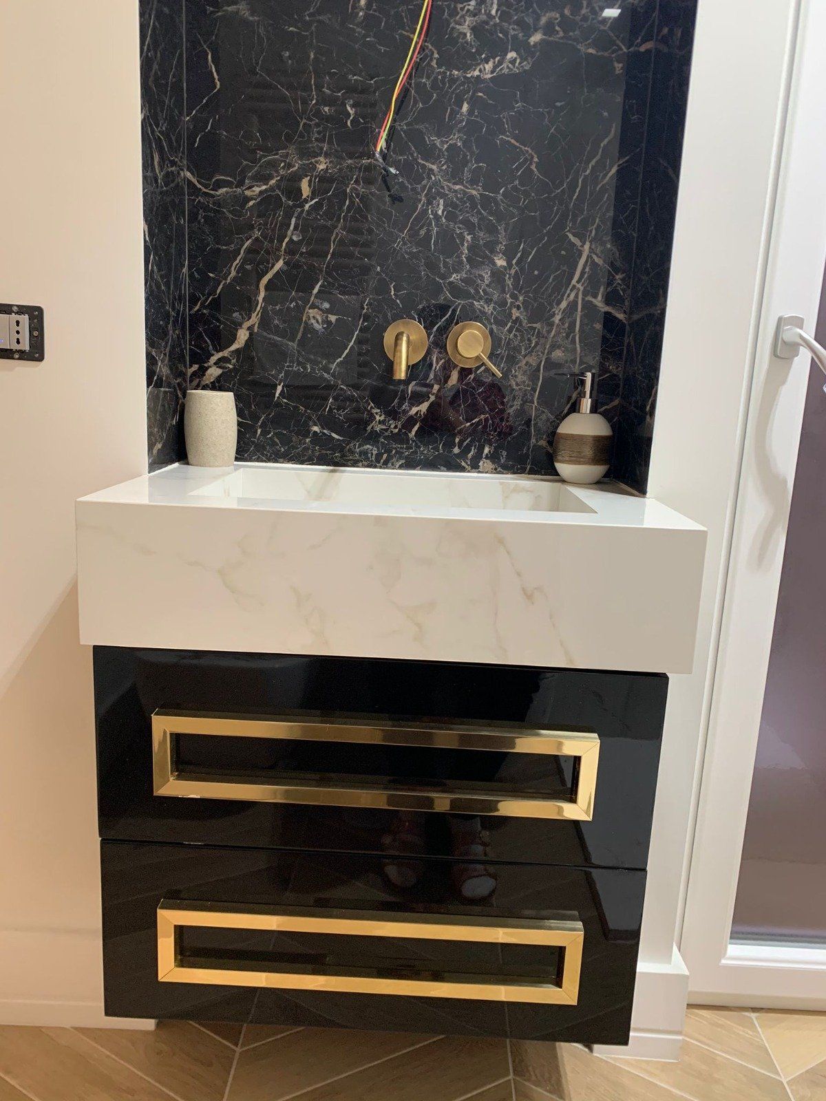 Un lavandino del bagno con un mobiletto nero e maniglie dorate.
