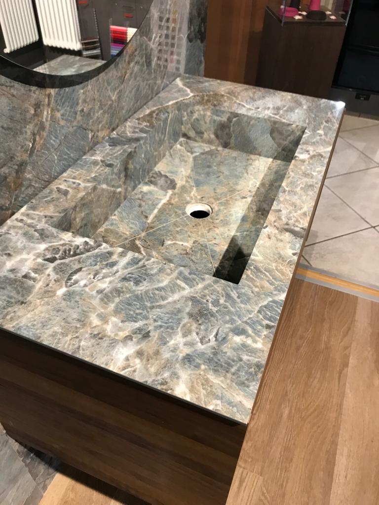 Un lavandino del bagno con un piano in marmo e un mobiletto in legno.