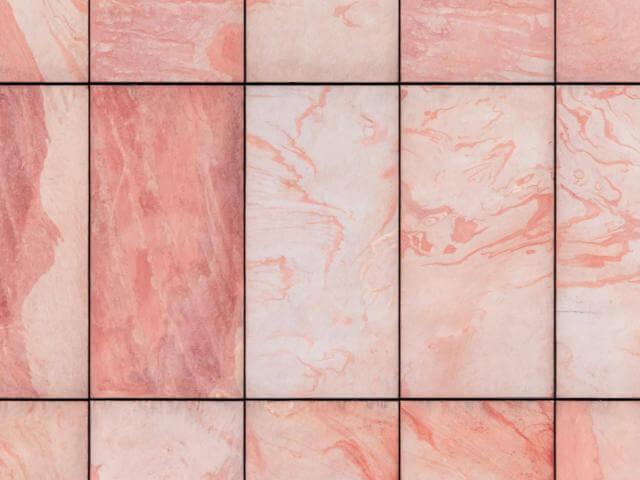 Un primo piano di una parete rivestita di piastrelle di marmo rosa.