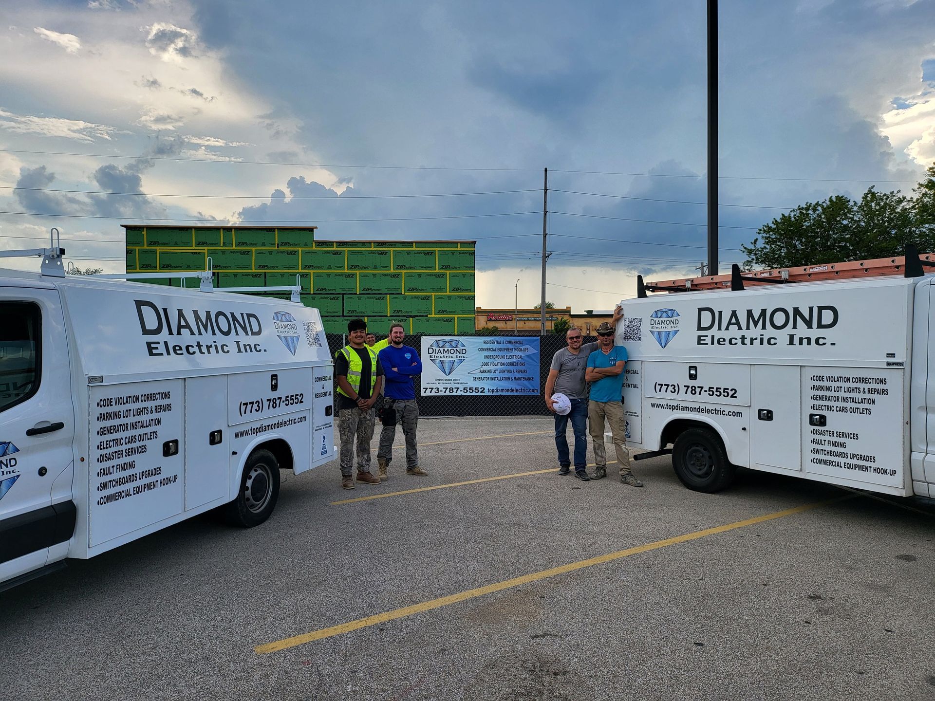 A group of men standing next to a diamond electric truck in a parking lot.