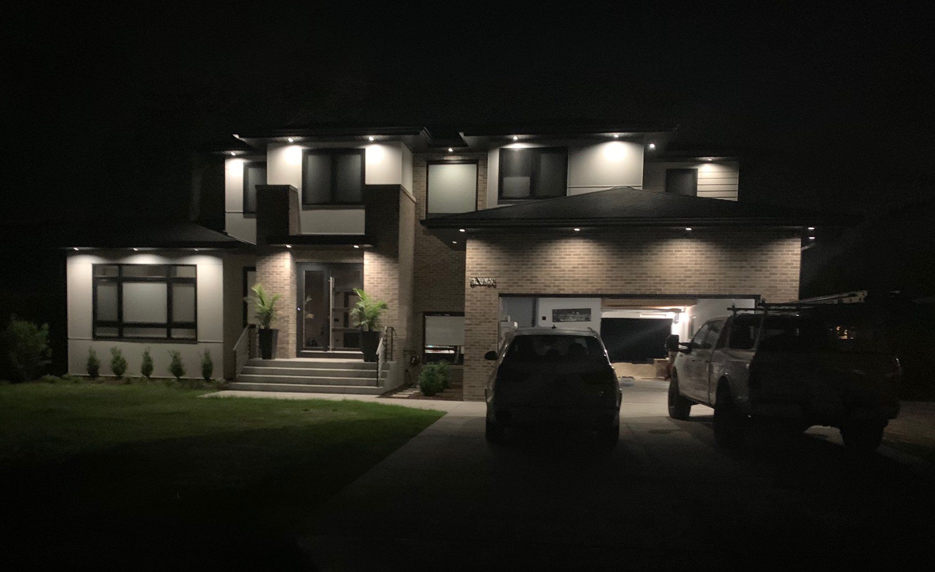 Two cars are parked in front of a house at night.