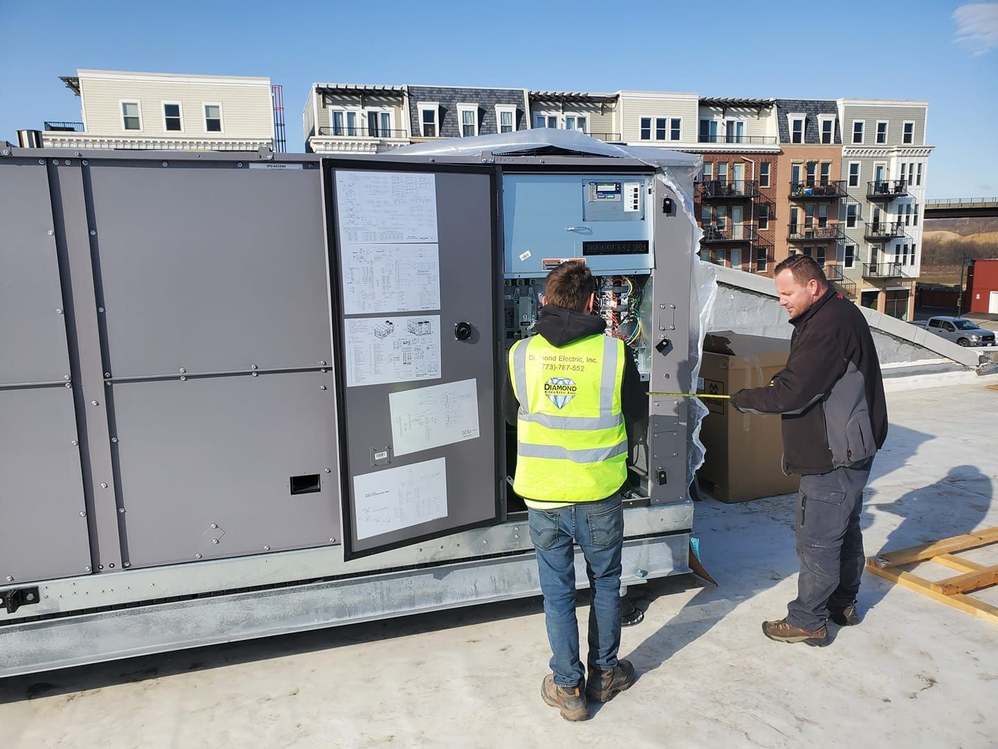Two men are working on a roof with a building in the background.