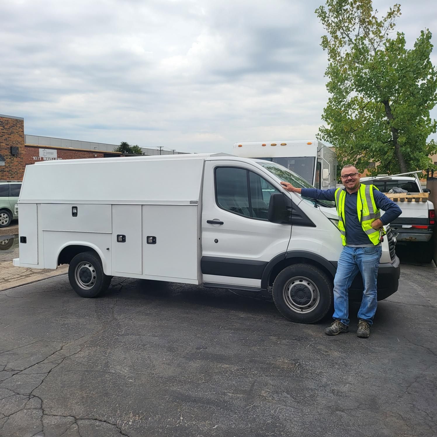 A man in a yellow vest is standing next to a white van.