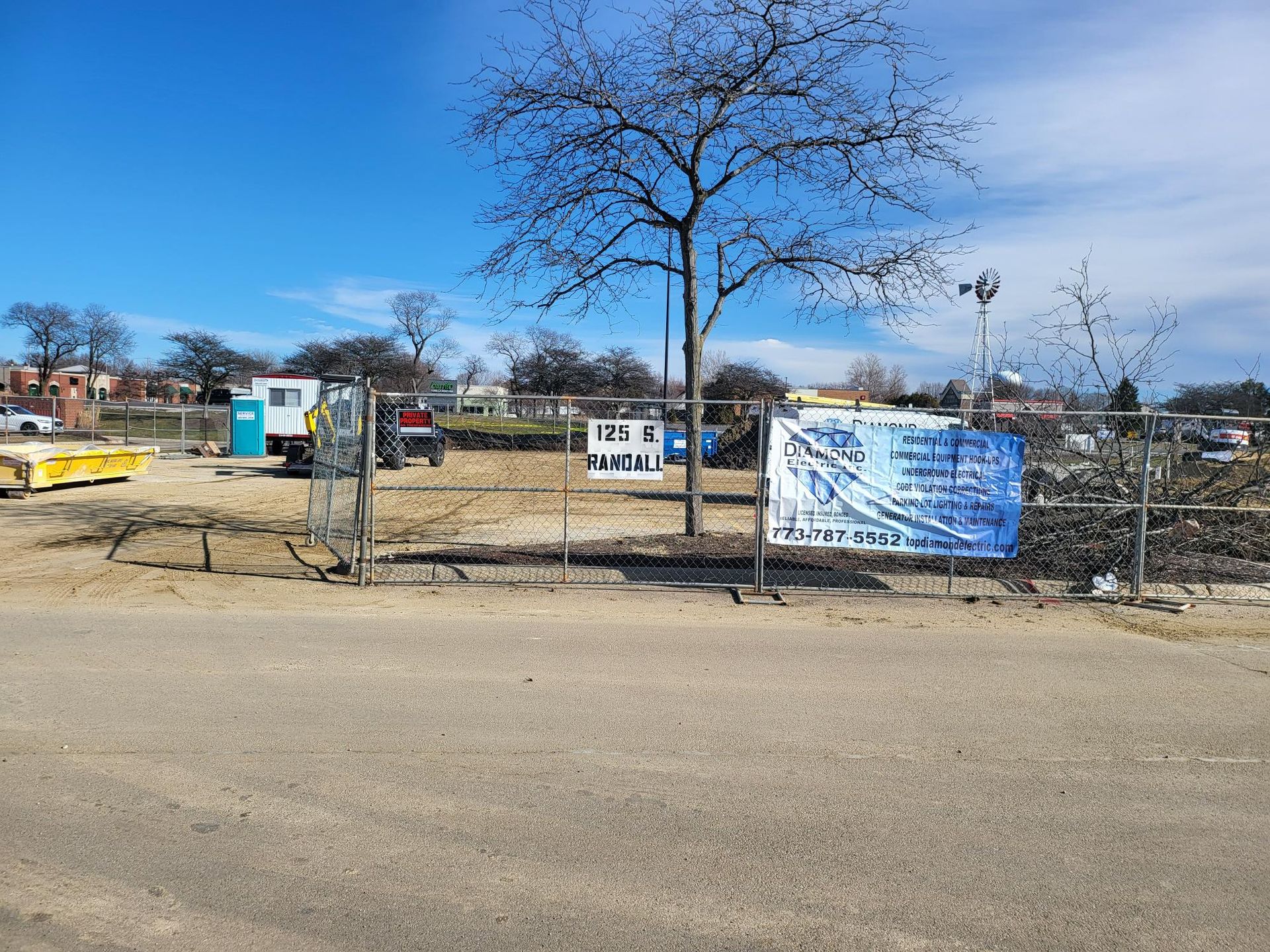 A construction site with a fence and a tree in the background.