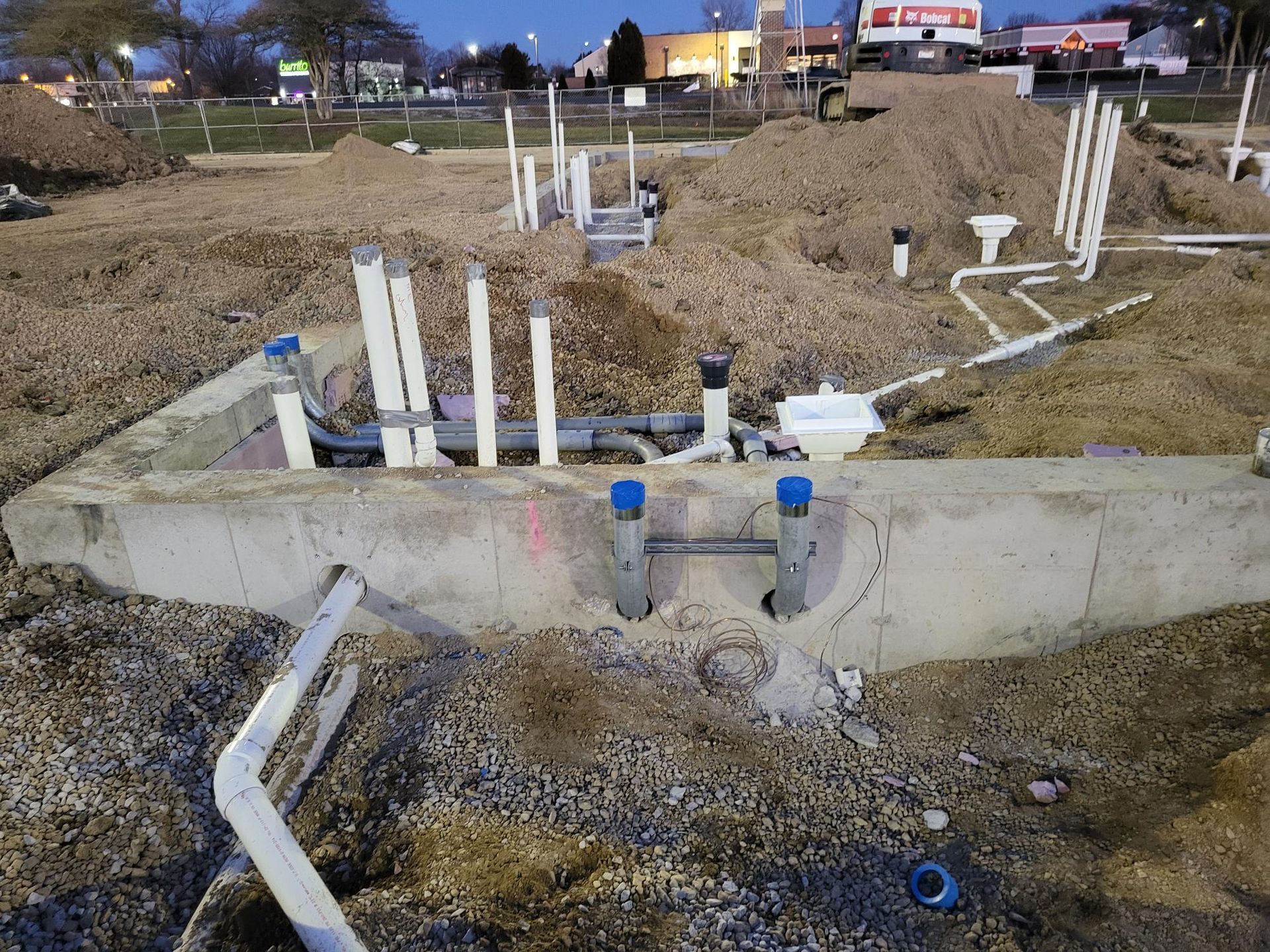 A bunch of pipes are laying in the dirt on a construction site.