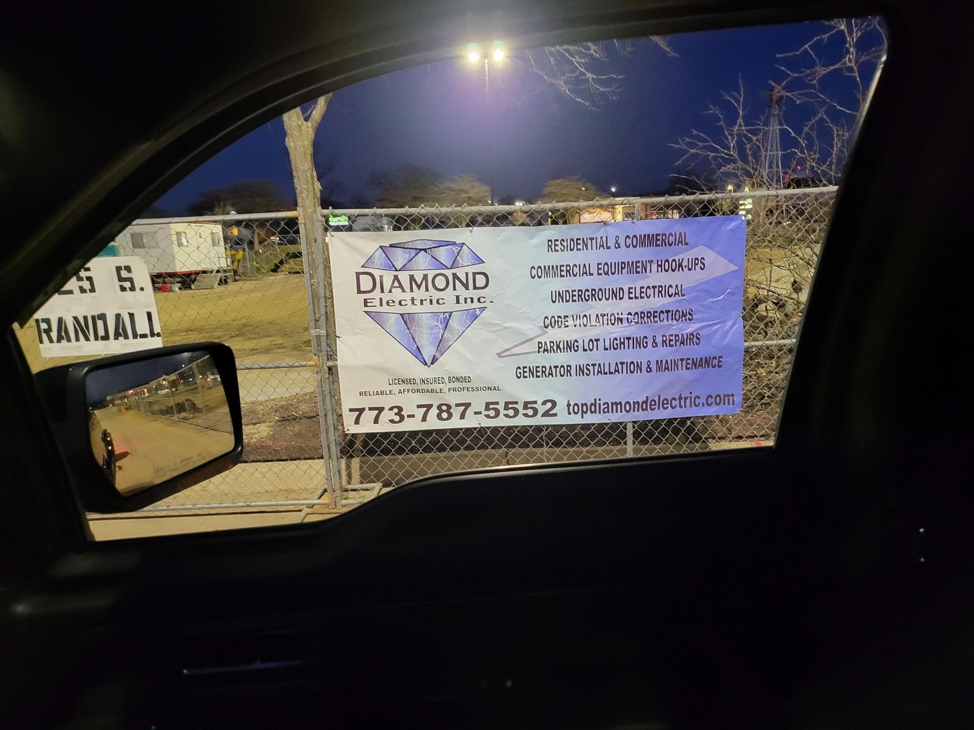 A car is parked in front of a diamond fence company sign.