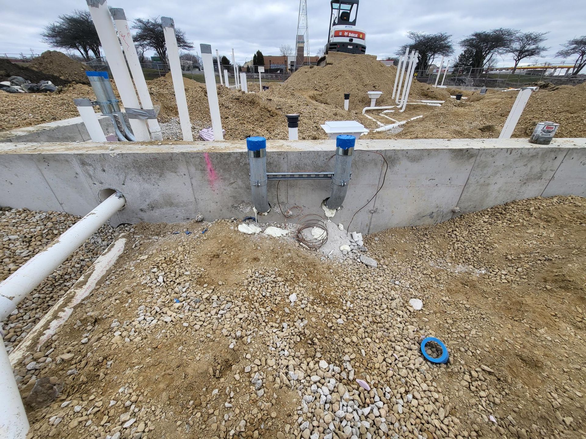 A construction site with a concrete wall and pipes in the dirt.
