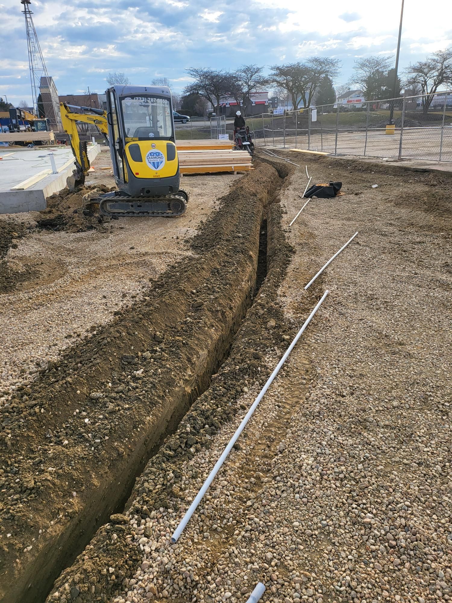 A yellow excavator is digging a trench in the dirt on a construction site.