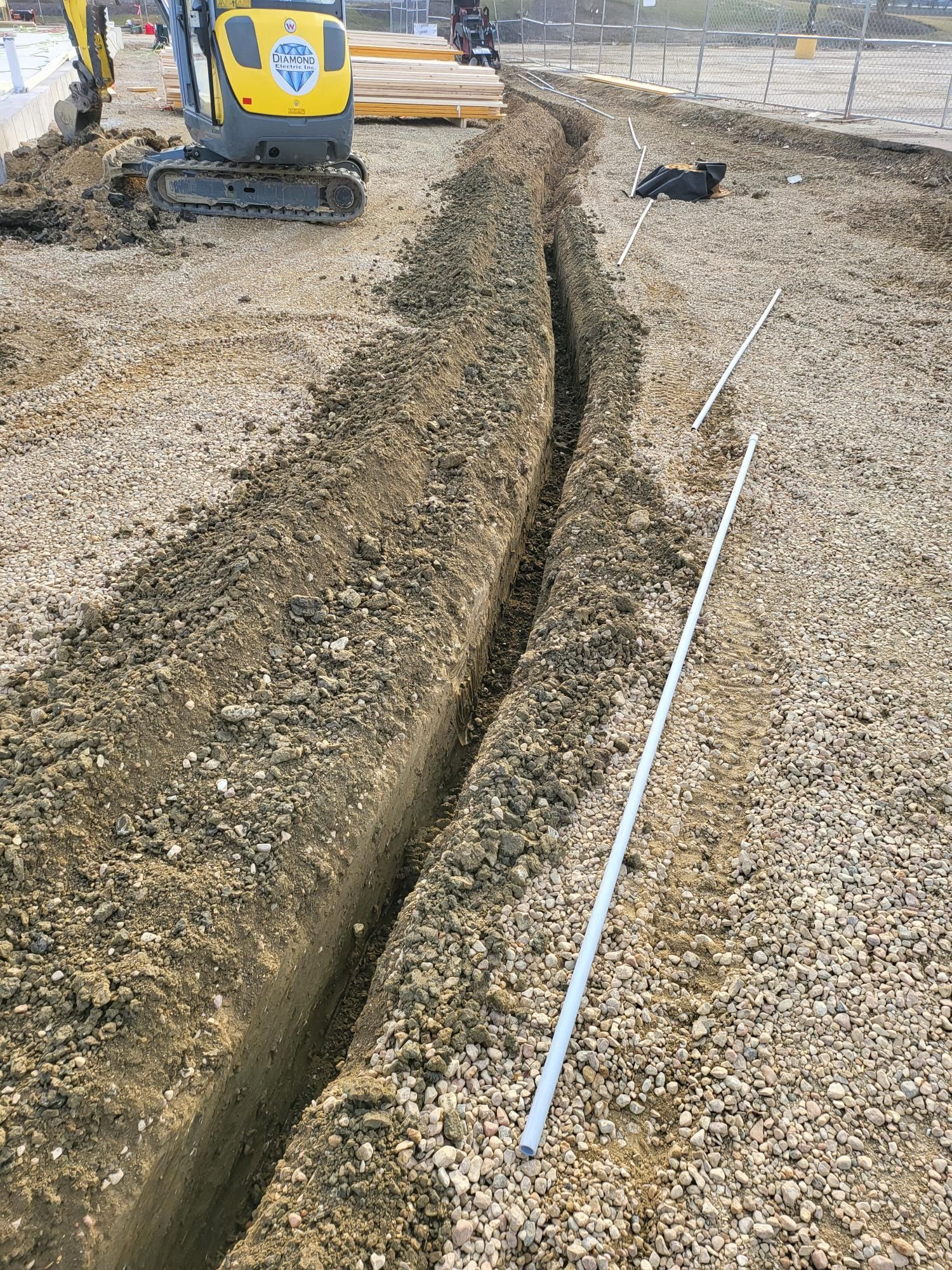 A yellow excavator is digging a trench in the dirt.