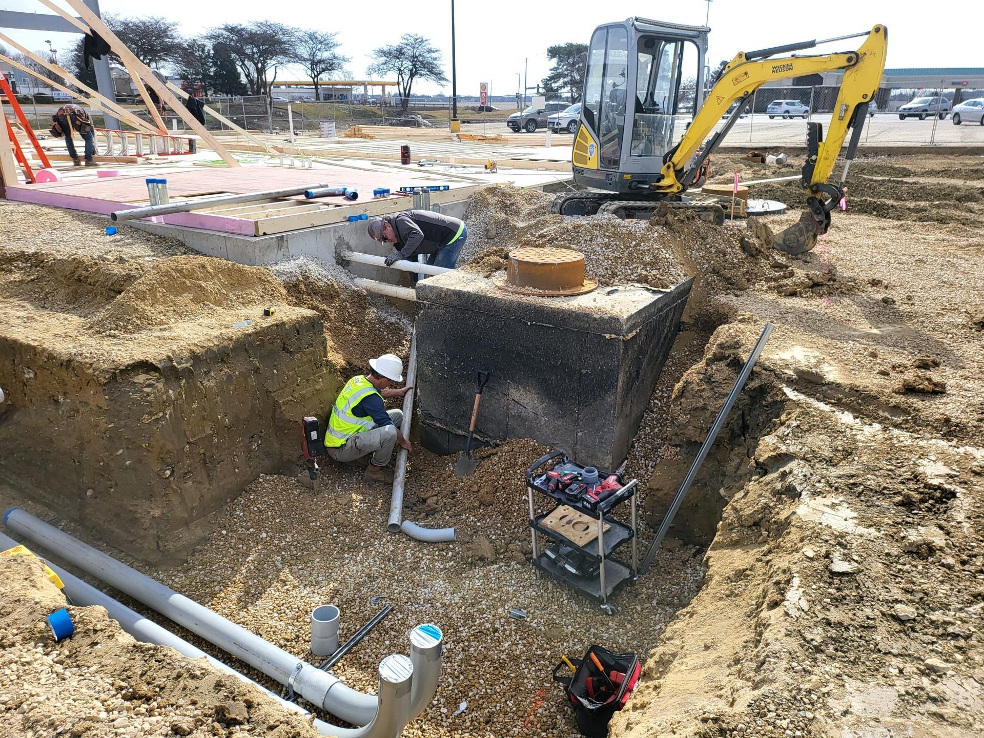 A construction worker is kneeling in the dirt in front of a yellow excavator.