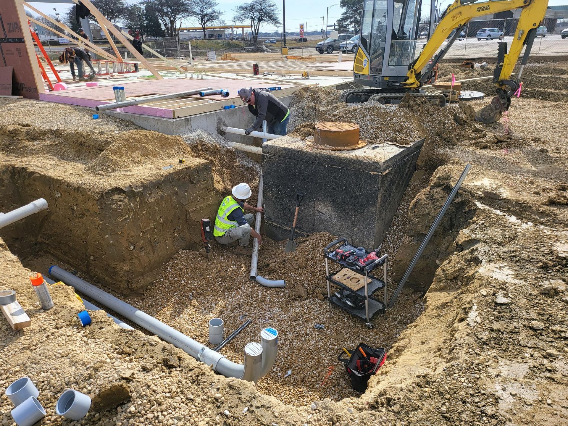 A construction site with a yellow excavator and a man kneeling in the dirt.
