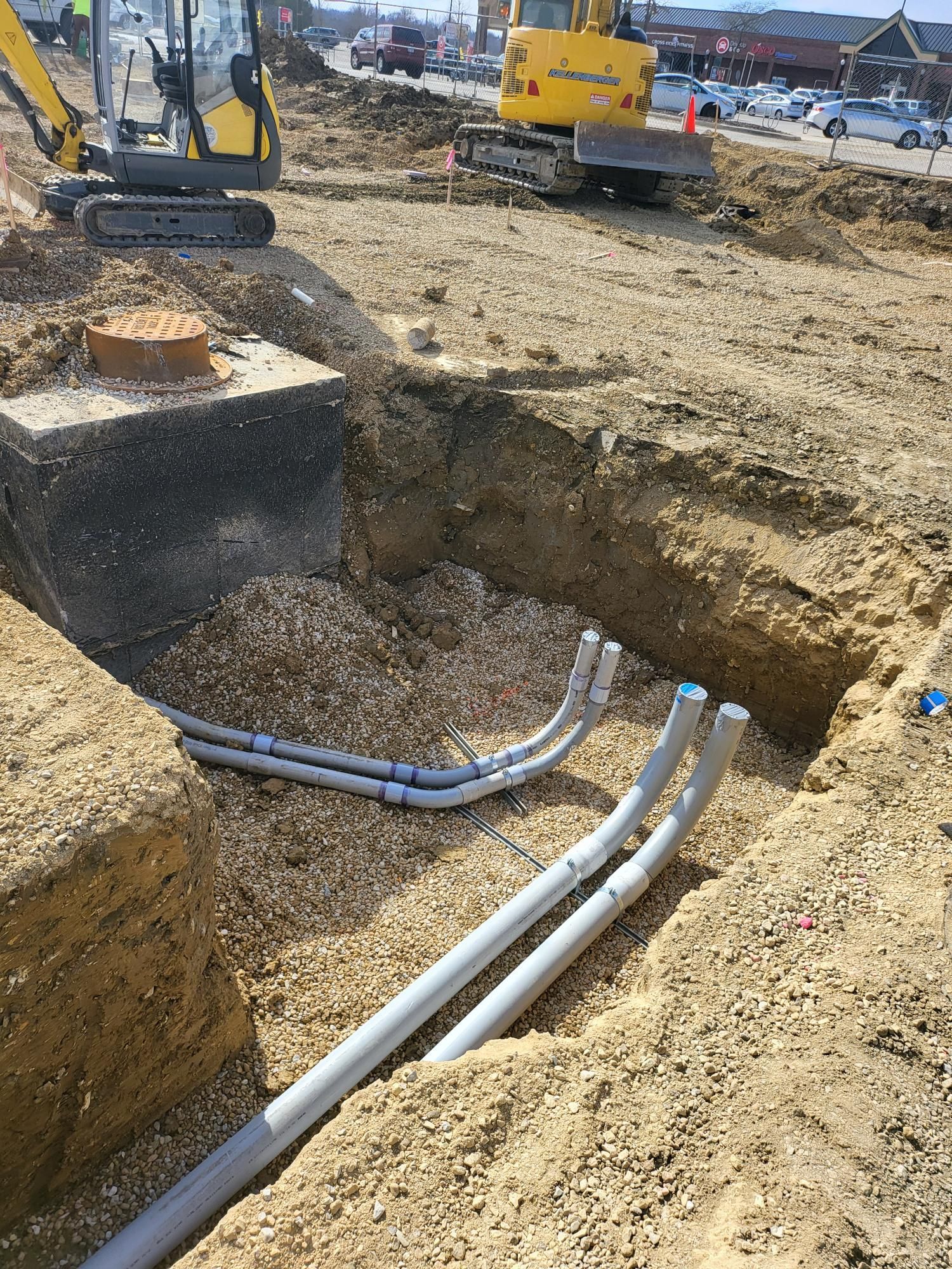 A construction site with a yellow excavator and a bunch of pipes in the dirt.