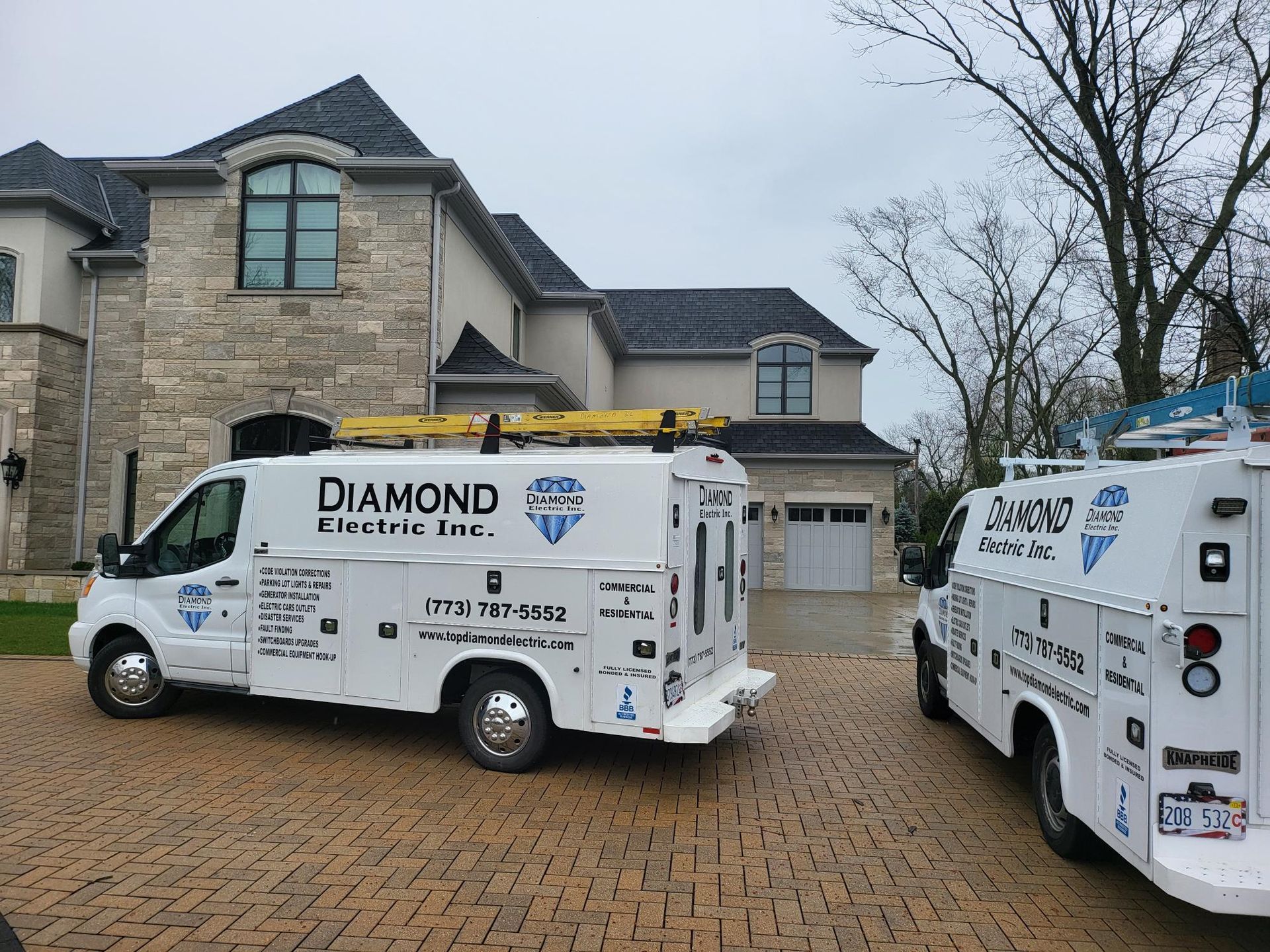 Two diamond electric vans are parked in front of a large house.