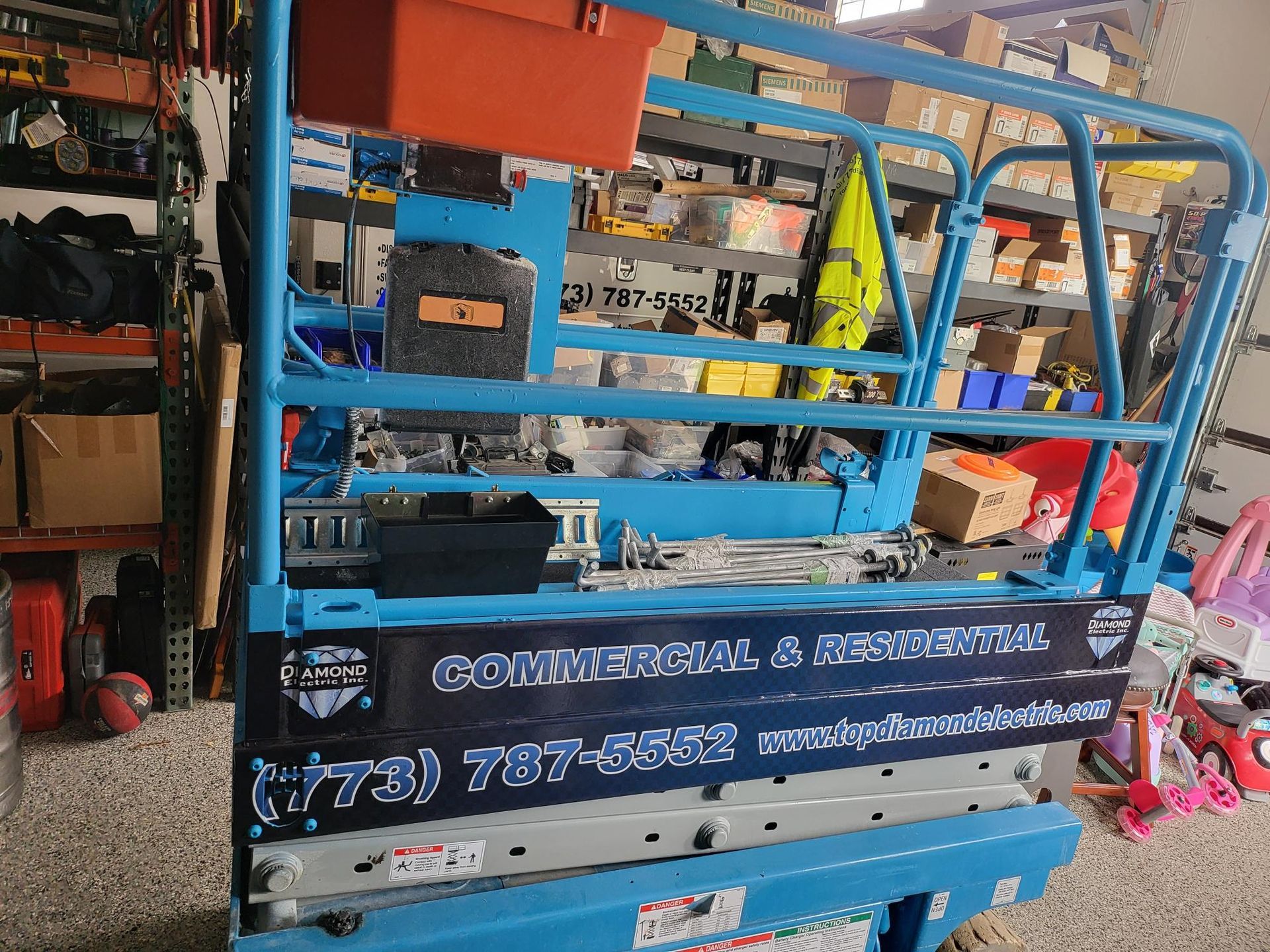 A blue scissor lift is sitting in a warehouse.