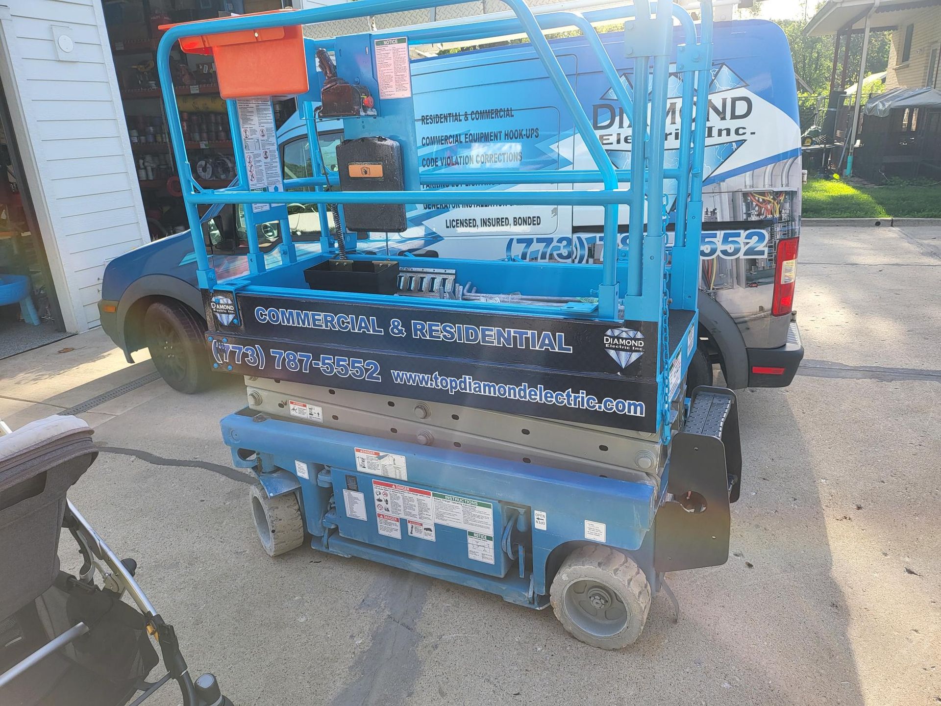 A blue van is parked next to a blue scissor lift.