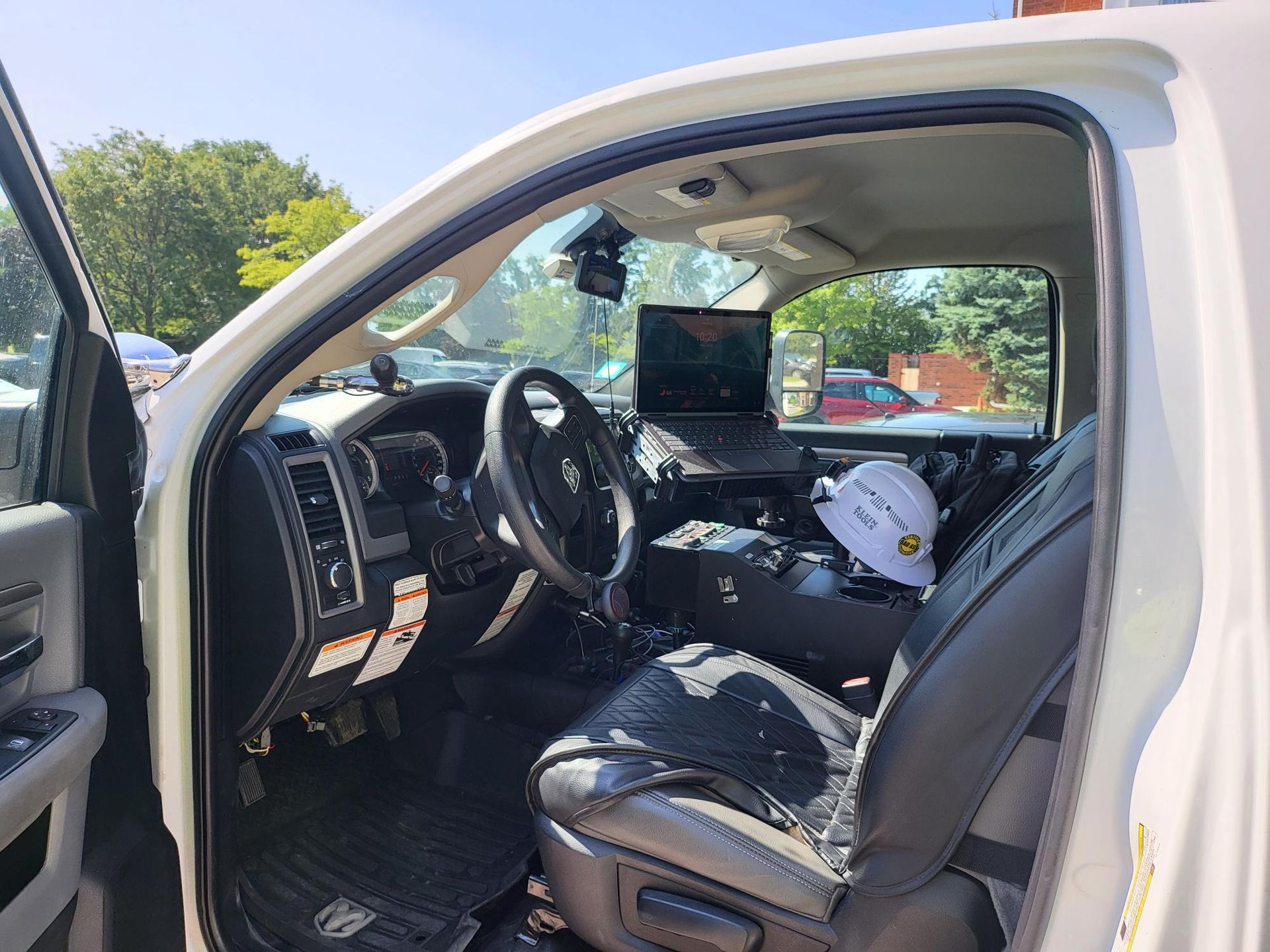 The inside of a white truck with the door open and a laptop on the dashboard.