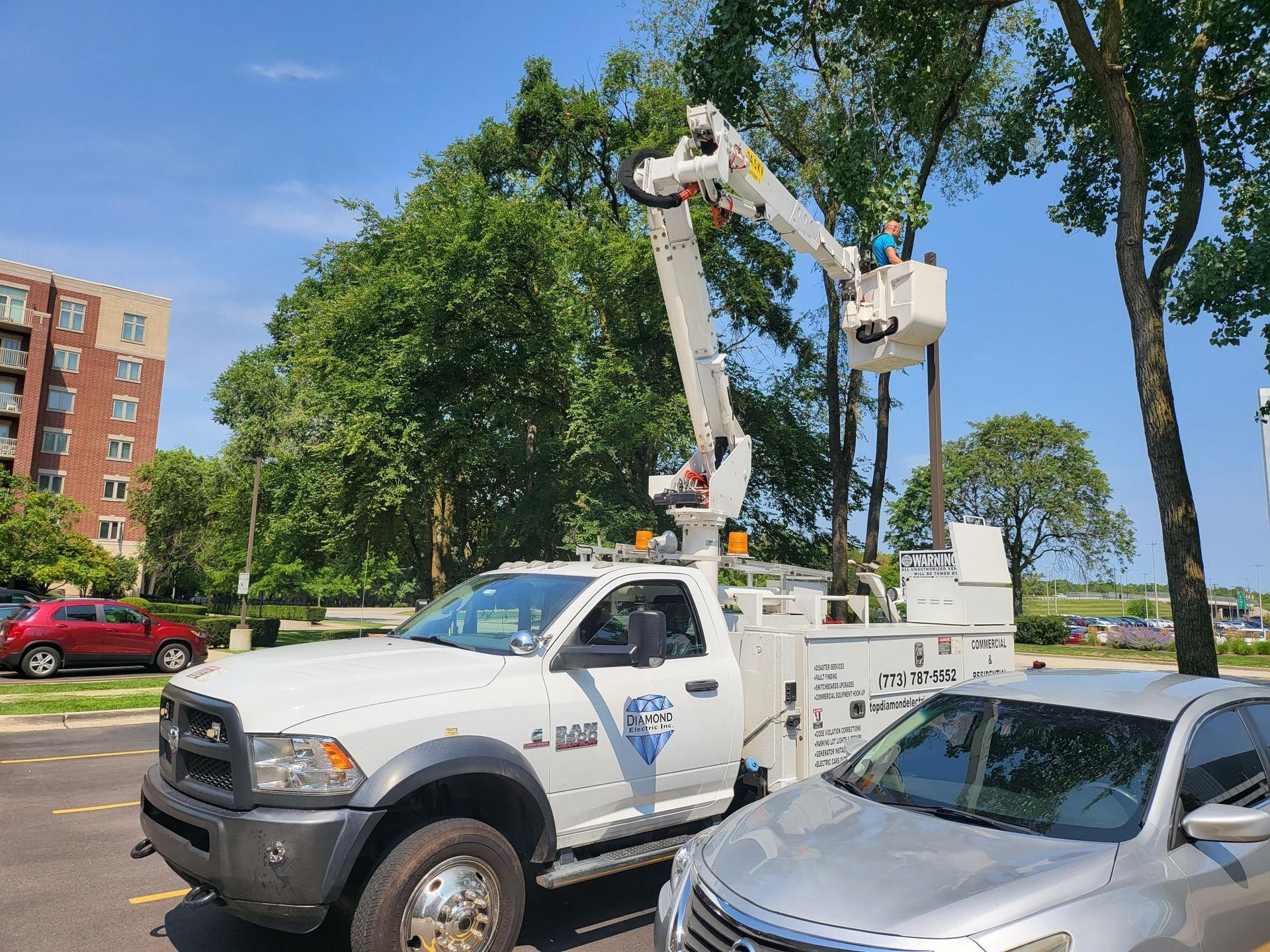 A white truck with a crane on the back is parked next to a silver car.