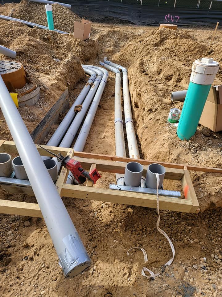 A bunch of pipes are laying in the dirt on a construction site.