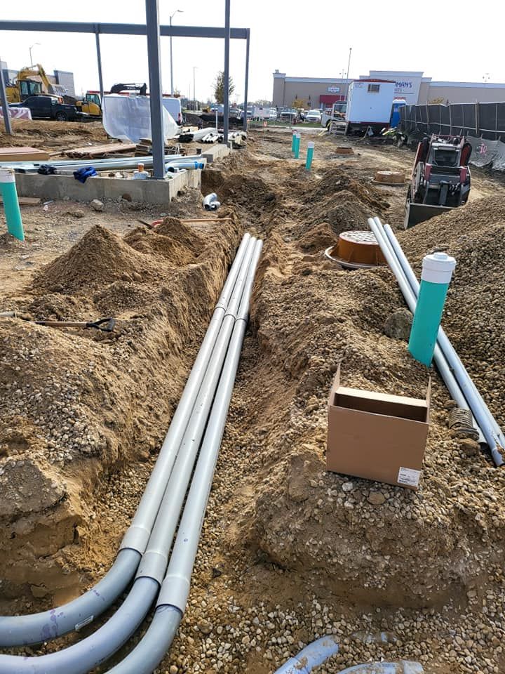 A bunch of pipes are laying in the dirt on a construction site.