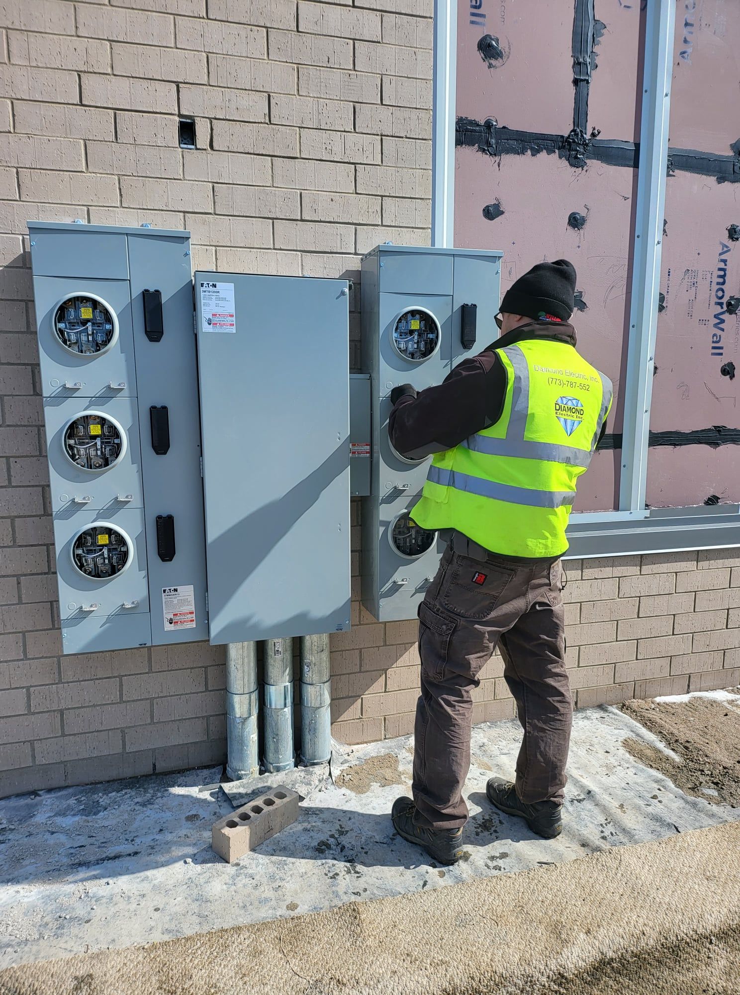 A man in a yellow vest is working on a meter on the side of a building.