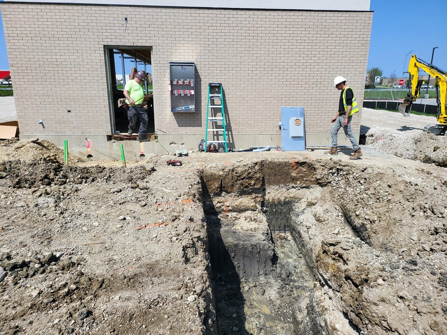 A construction site with a hole in the ground in front of a building.