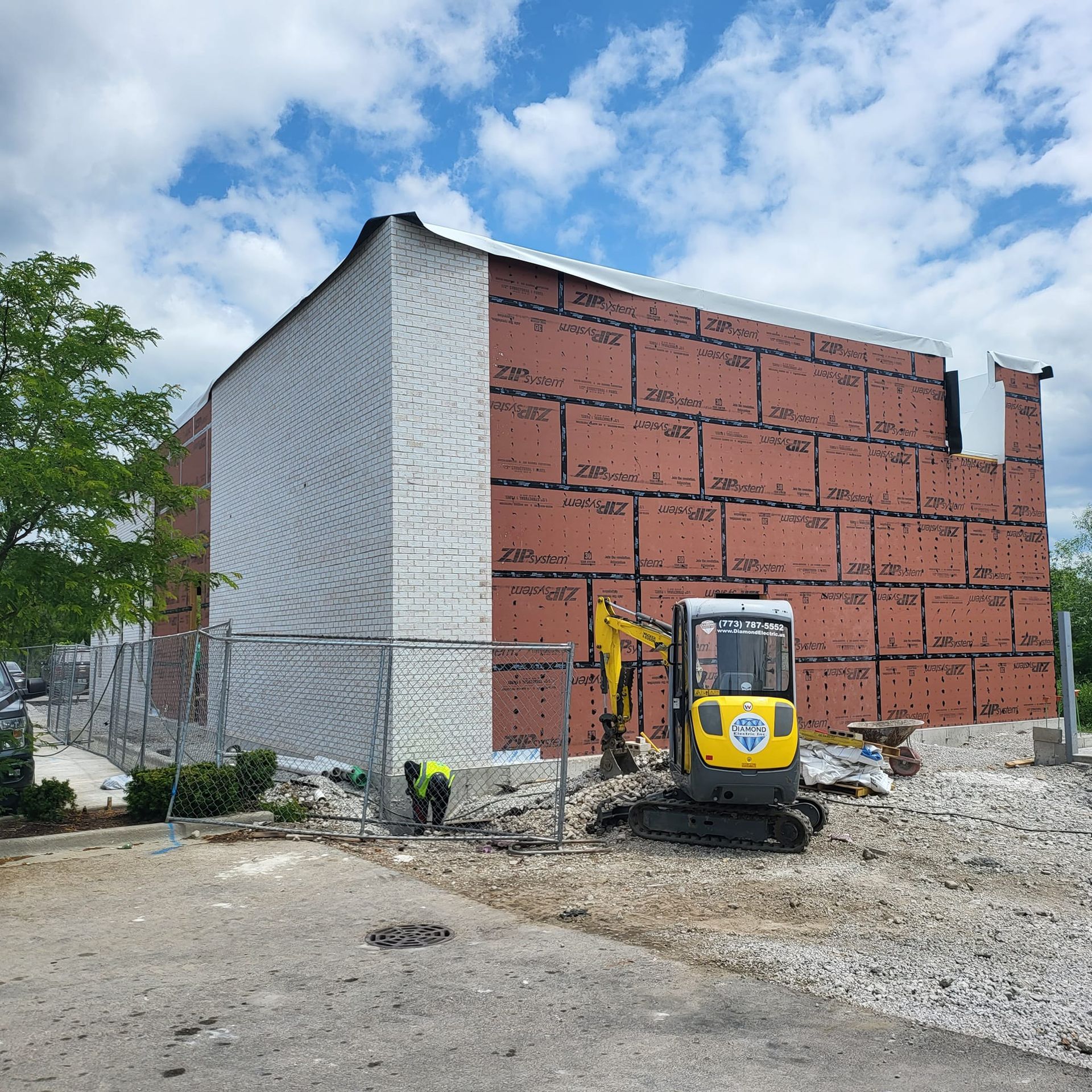 A yellow excavator is parked in front of a large brick building.