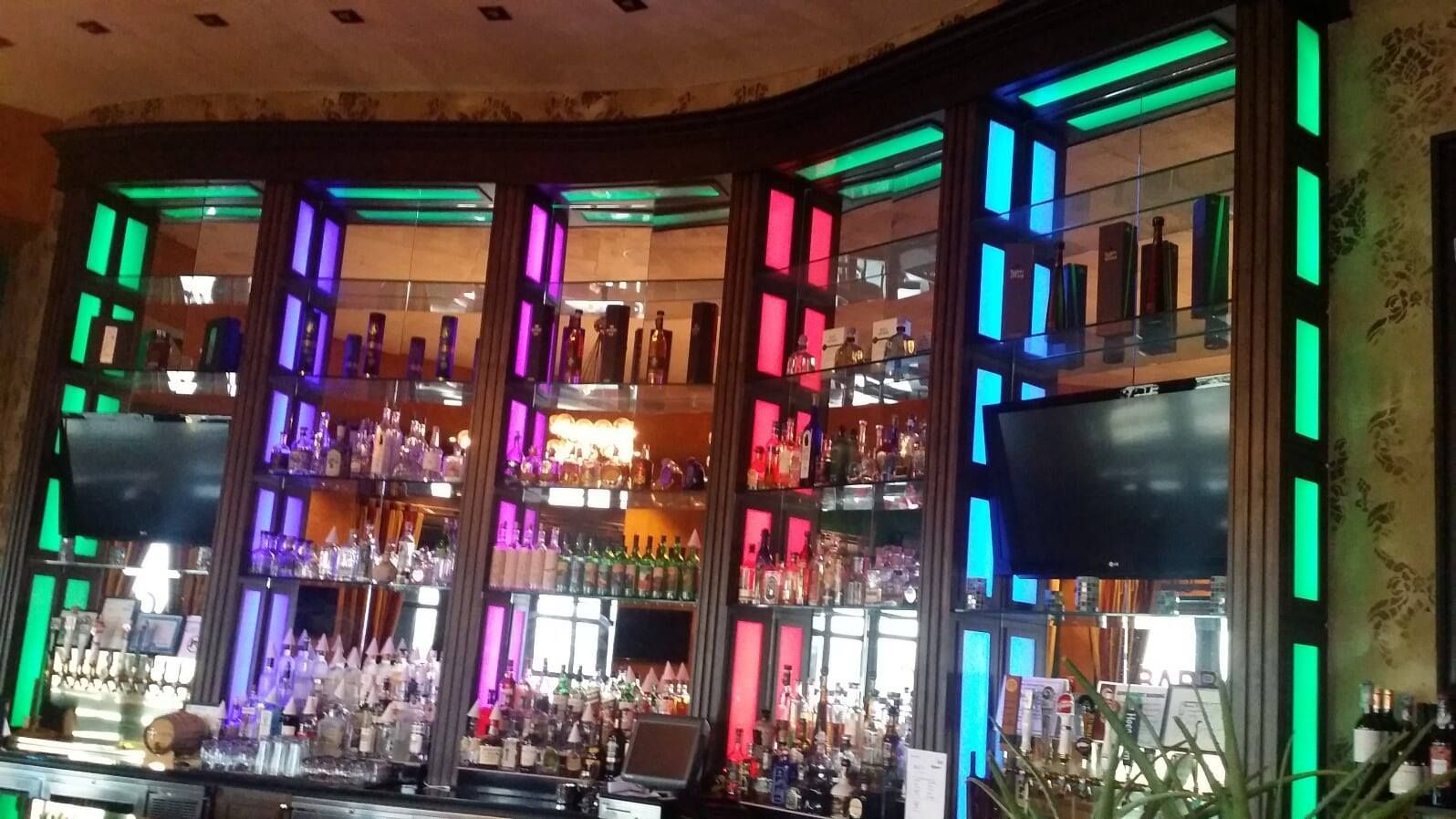 A bar with a lot of bottles of alcohol and a tv on the wall.