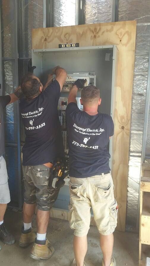Two men are working on a electrical box in a room.