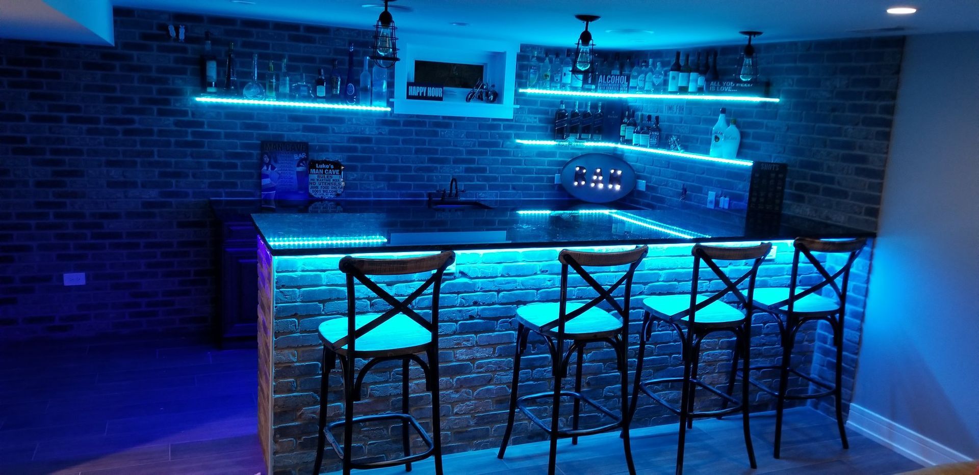 A bar in a basement with blue lights and stools.