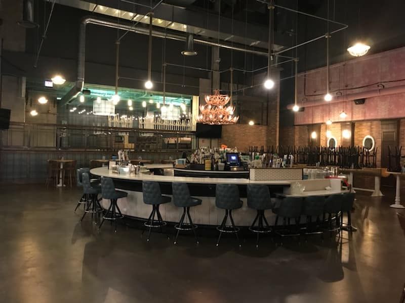 A large empty restaurant with a long bar and stools.