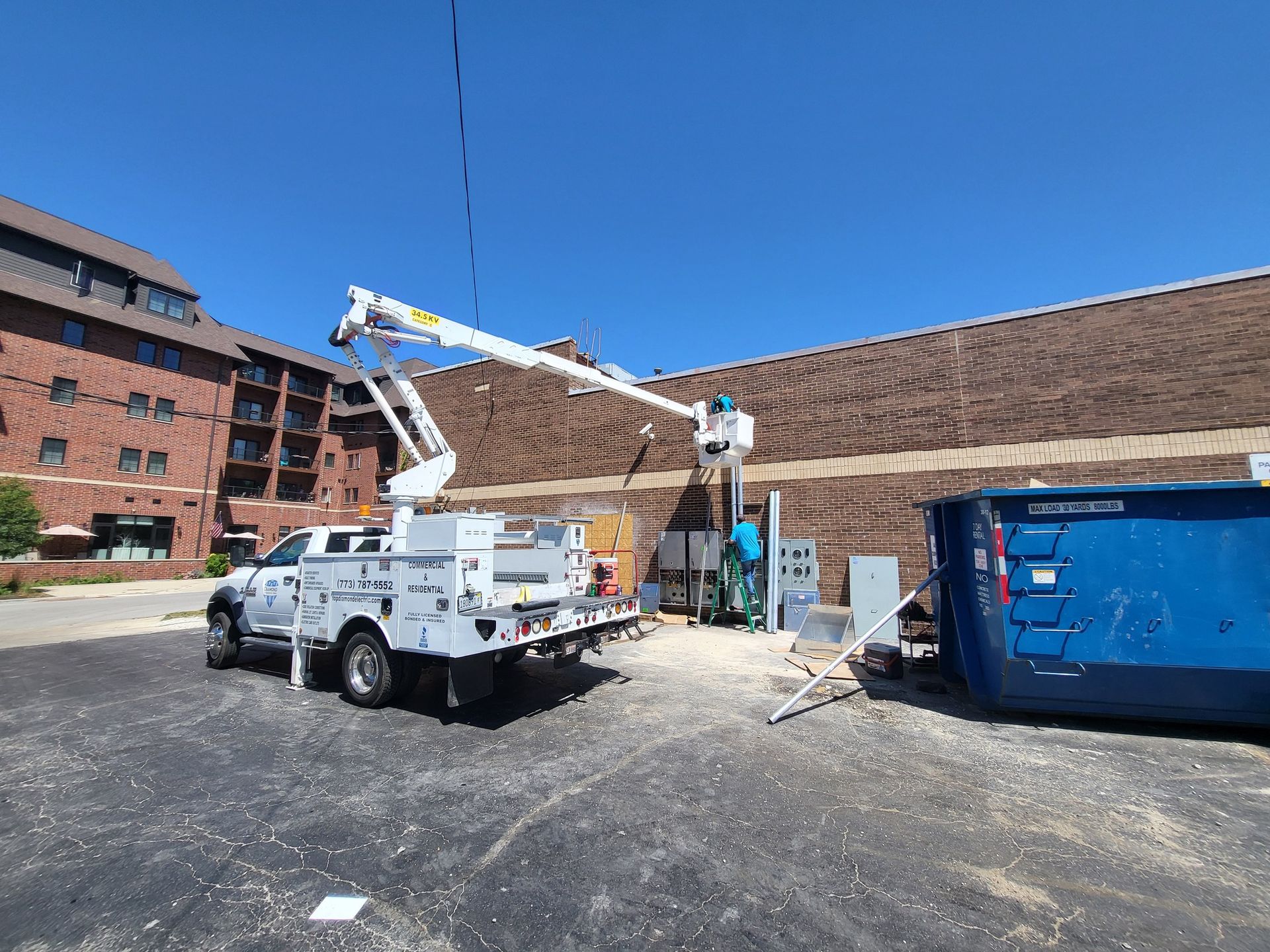 A white truck with a crane on the back is parked in front of a brick building.