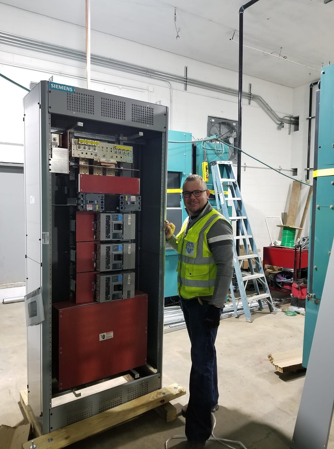 A man in a yellow vest is standing in front of a large electrical box.