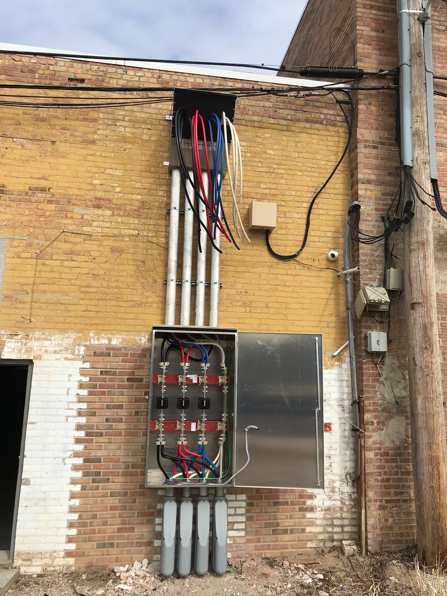 A large electrical box is attached to the side of a brick building.