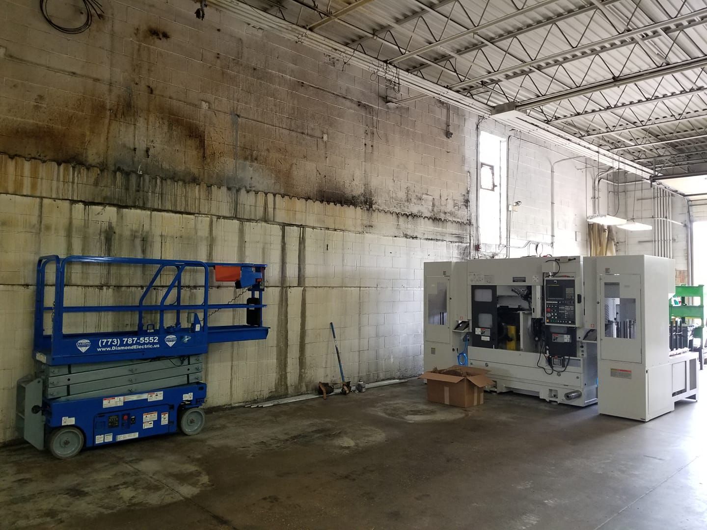A blue scissor lift is parked in a warehouse next to a machine.