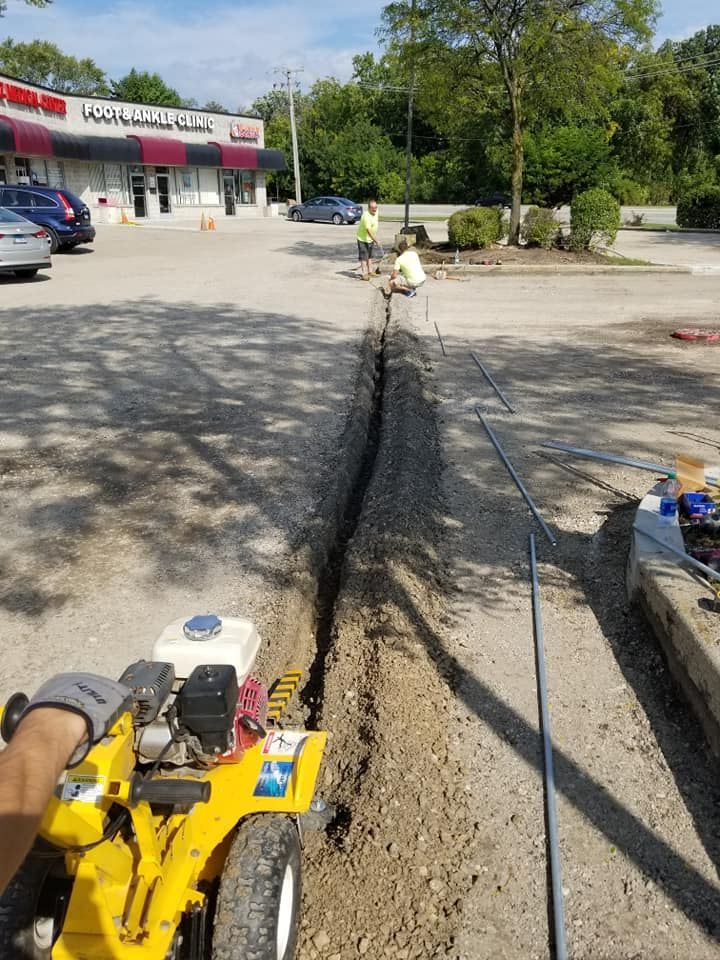 A yellow tractor is cutting a hole in the ground in a parking lot.