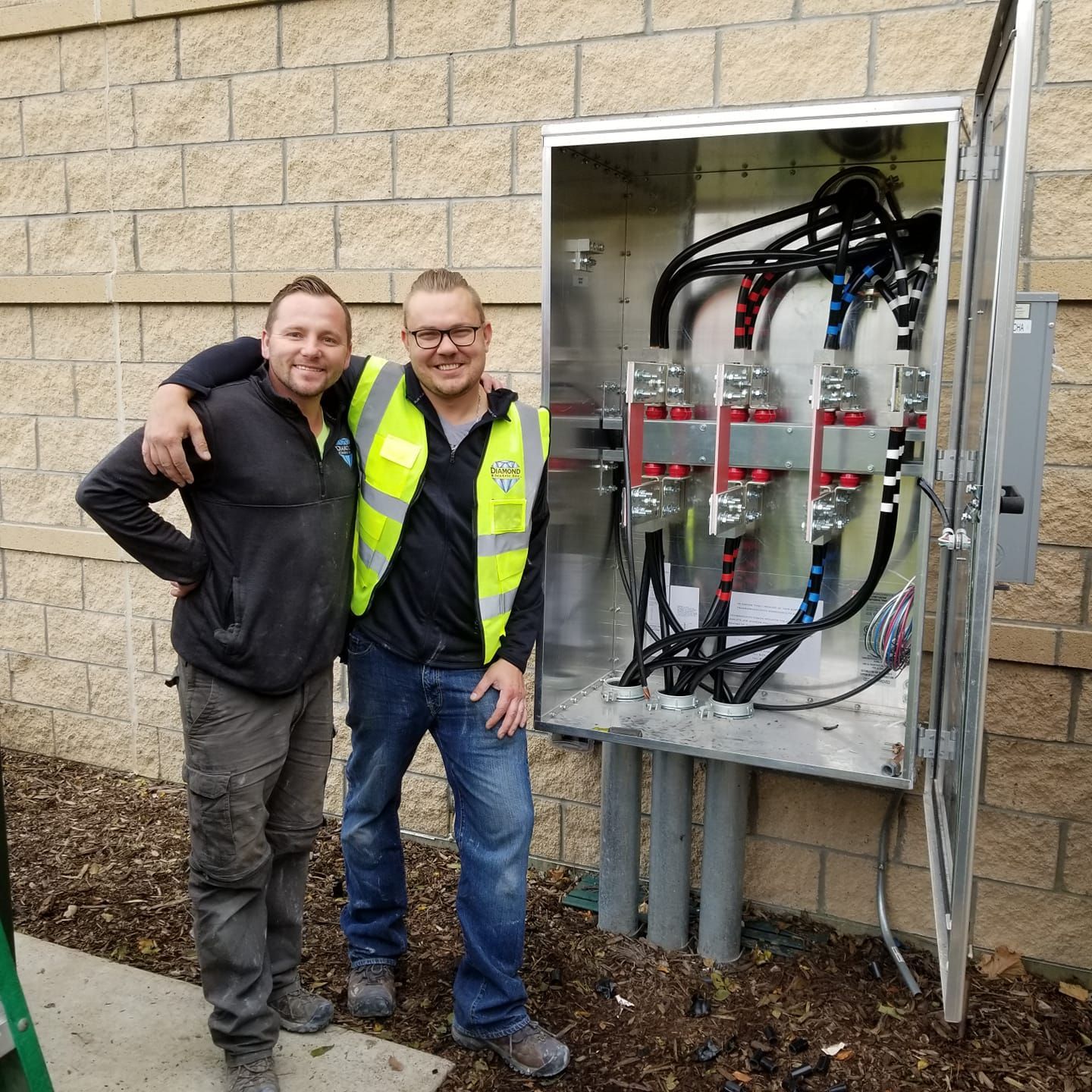 Two men are posing for a picture in front of an electrical box.