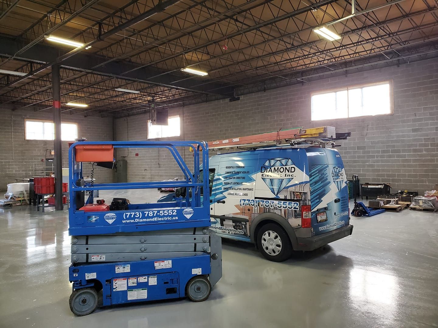 A van is parked next to a scissor lift in a warehouse.