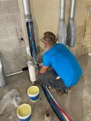 A man is kneeling down in a basement painting a pipe.