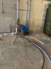 A man is kneeling on the floor in a room holding a hose.