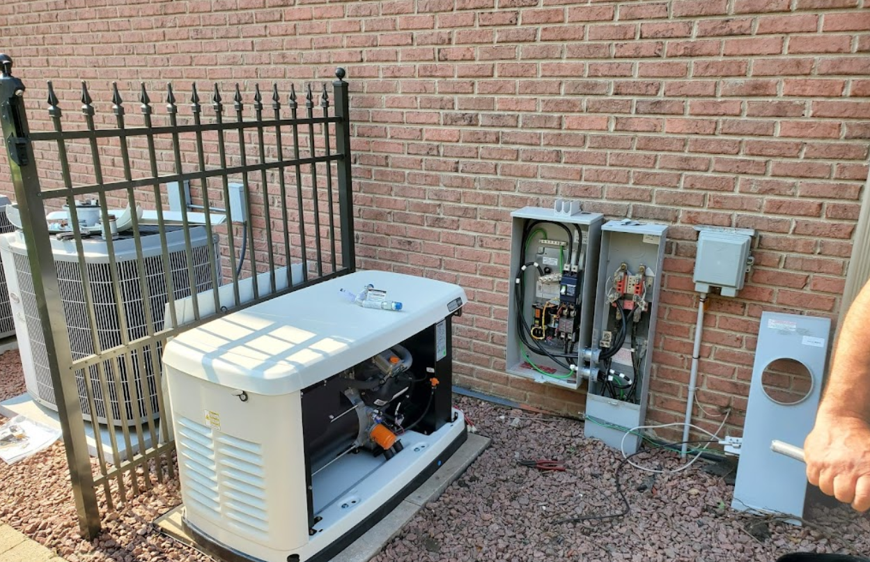 A generator is sitting outside of a brick building next to a fence.