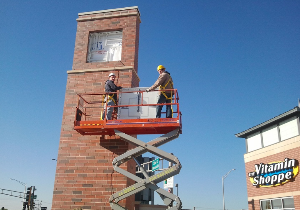 Two men are working on a brick tower in front of a vitamin shoppe