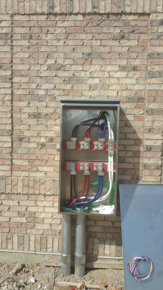 A large electrical box is attached to a brick wall.