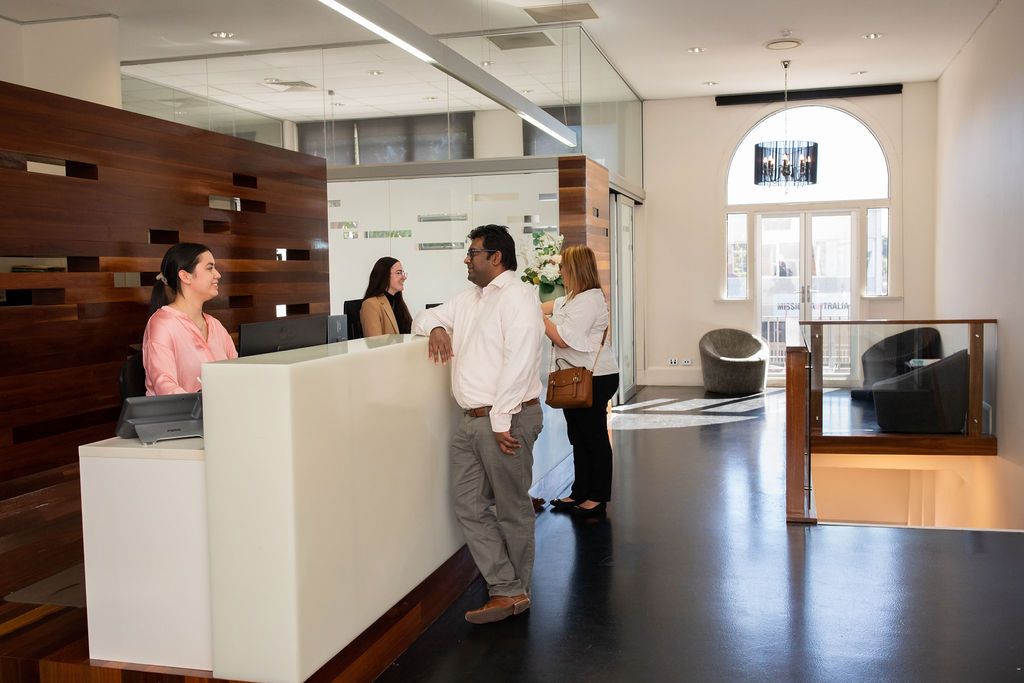 A group of people are standing at a reception desk in an office.