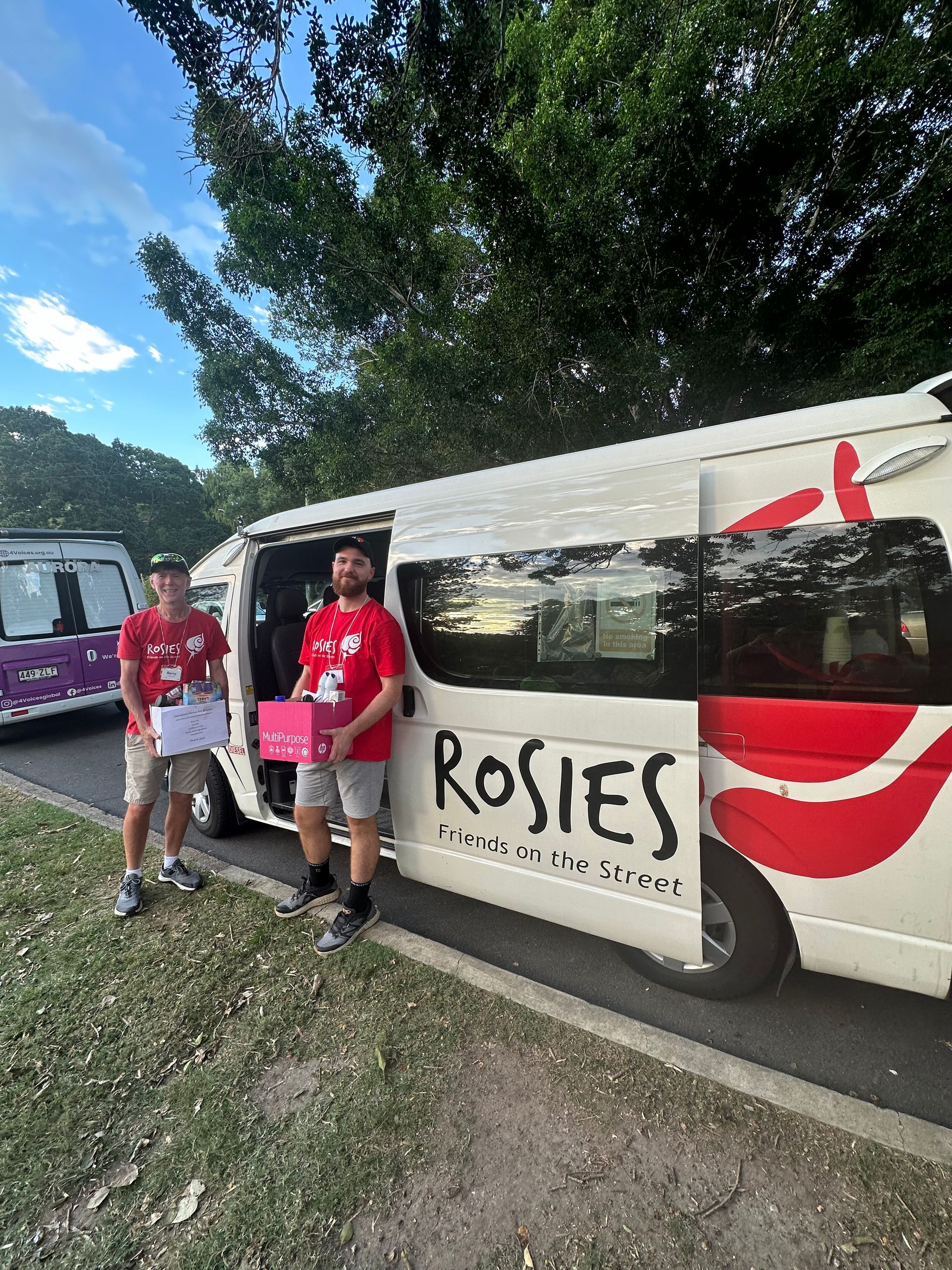 Two men are standing next to a white van that says rosies.
