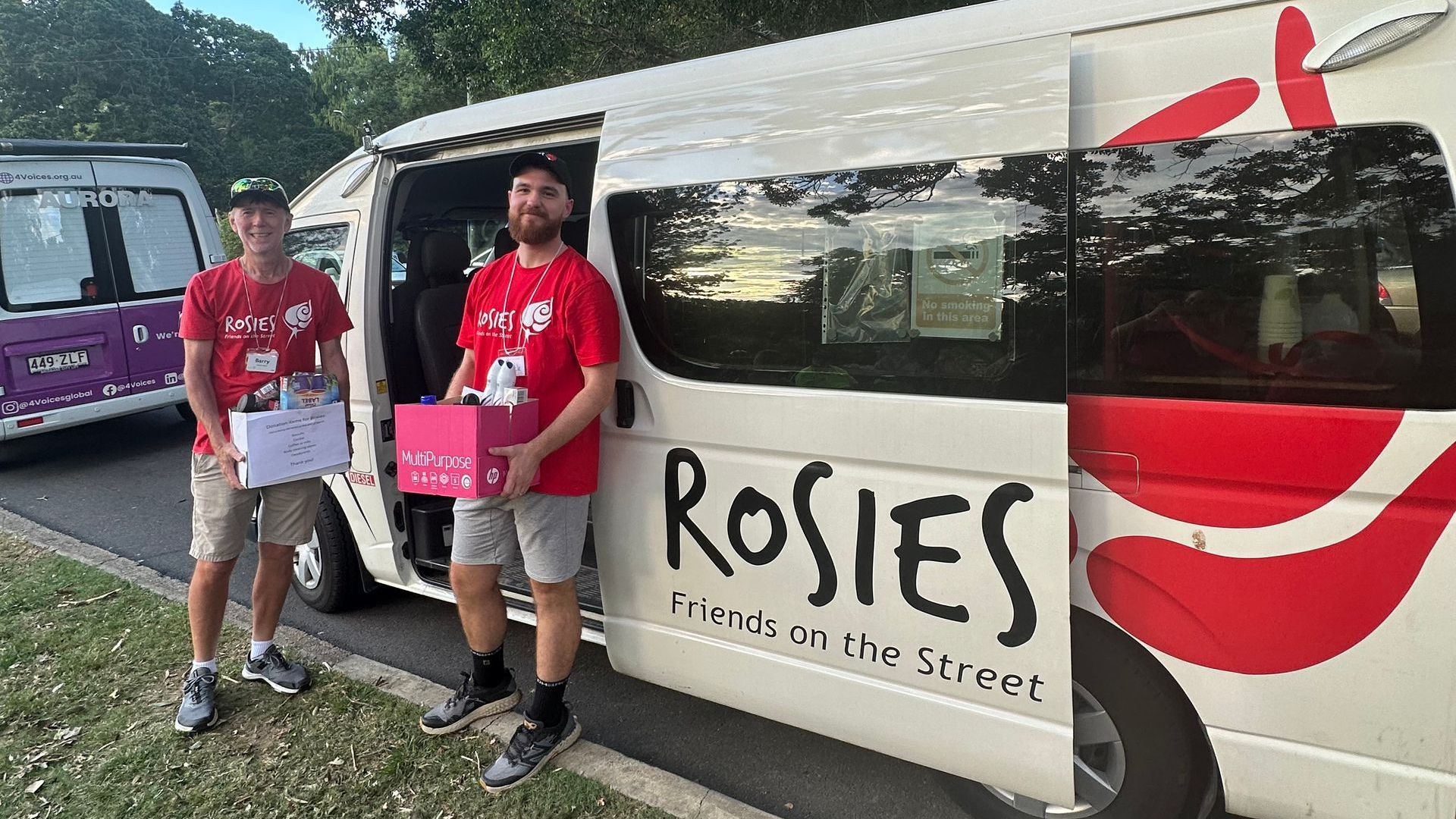 Two men are standing next to a white van that says rosies on the side.
