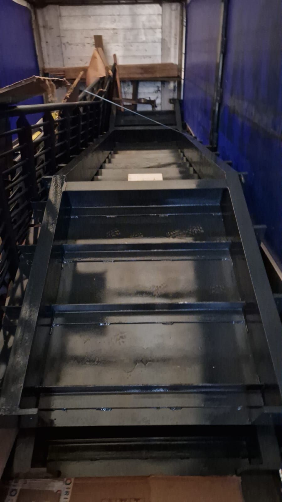 Vista dall'alto di una lunga piattaforma metallica nera all'interno di un edificio con pareti blu.